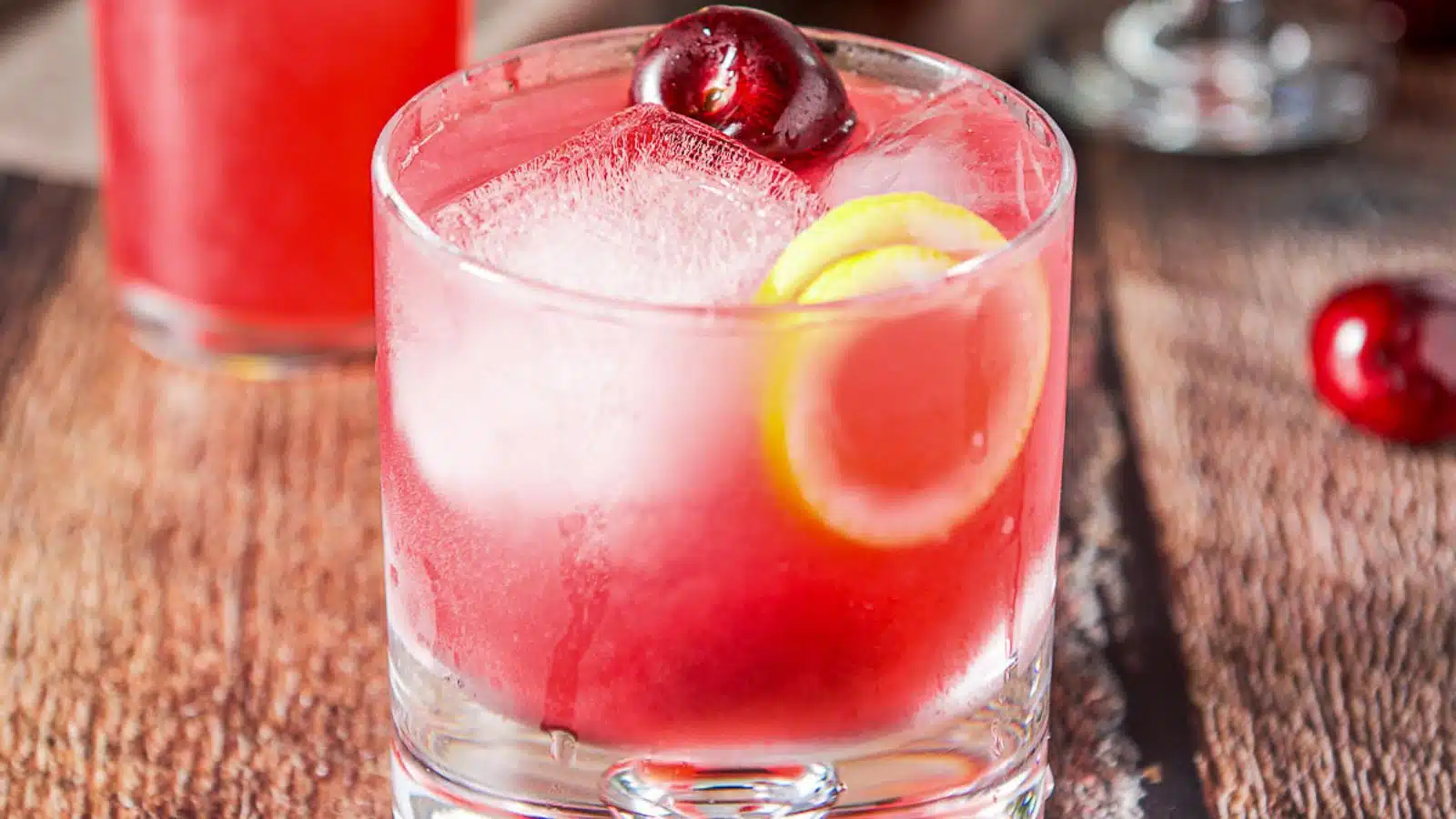 a glass with the cherry drink in it with a cherry and lemon twist in as garnish