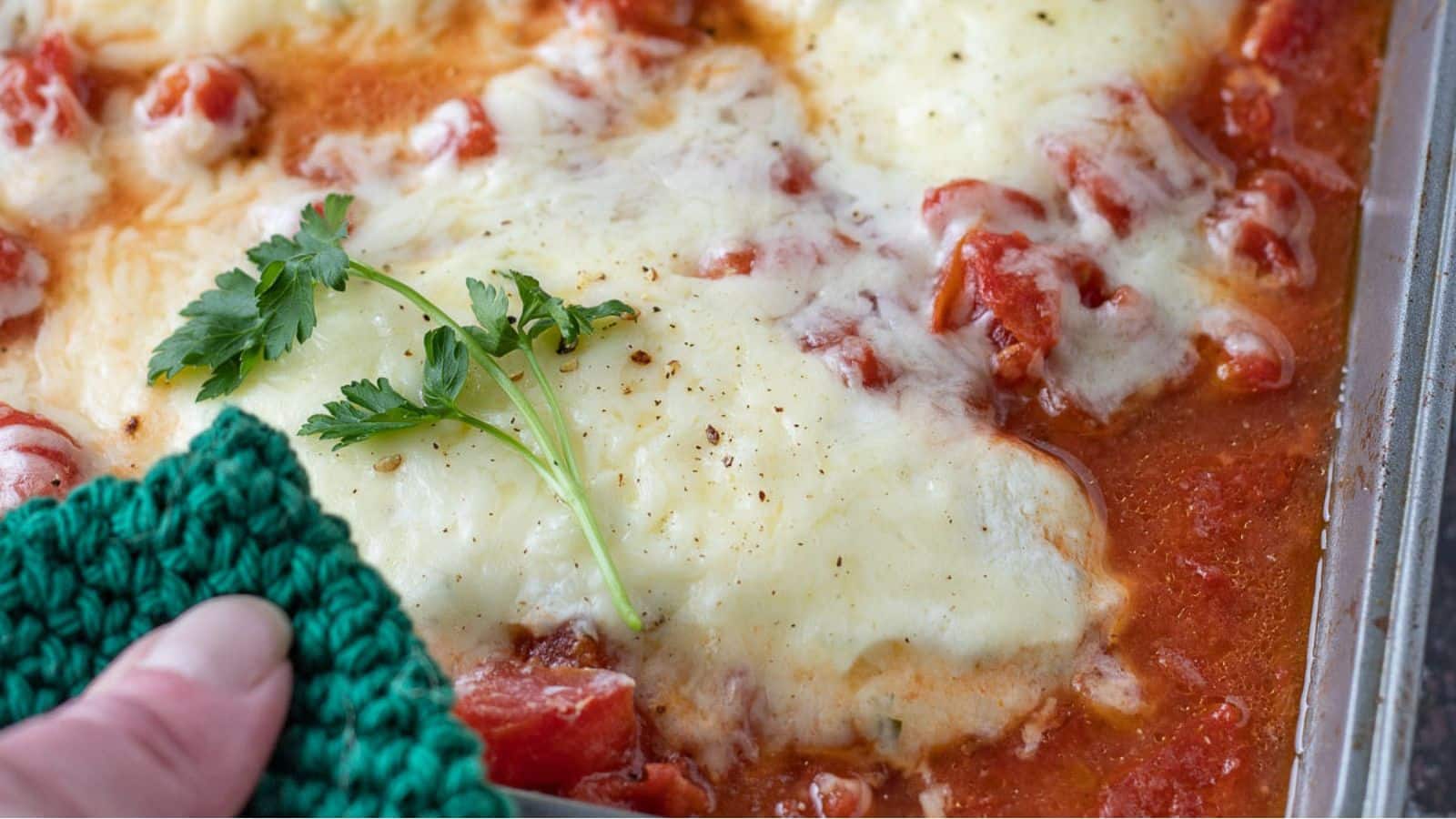 A pan of chicken with sauce and melted cheese and a sprig of parsley