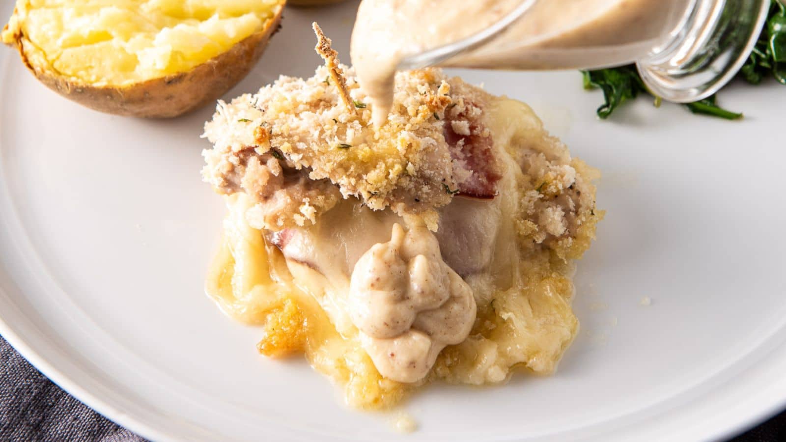 sauce being poured on the chicken stuffed with ham and cheese