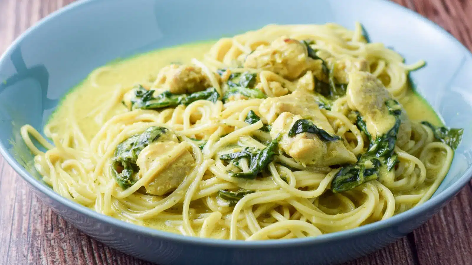 a blue green bowl filled with chicken, spinach, noodles and curry sauce