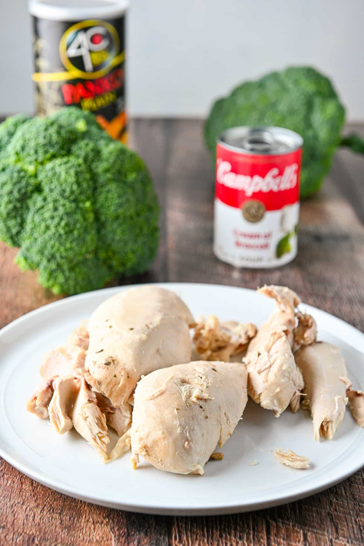 A white plate with cooked chicken breast on it, with broccoli, a can of soup, and panko bread crumbs in the back