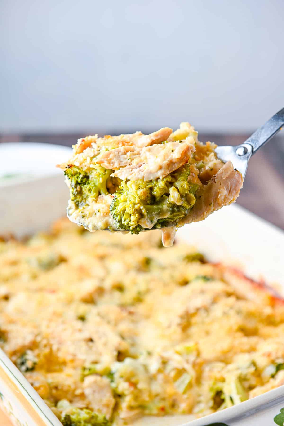 Chicken and broccoli in a big serving spoon held over the pan of chicken divan