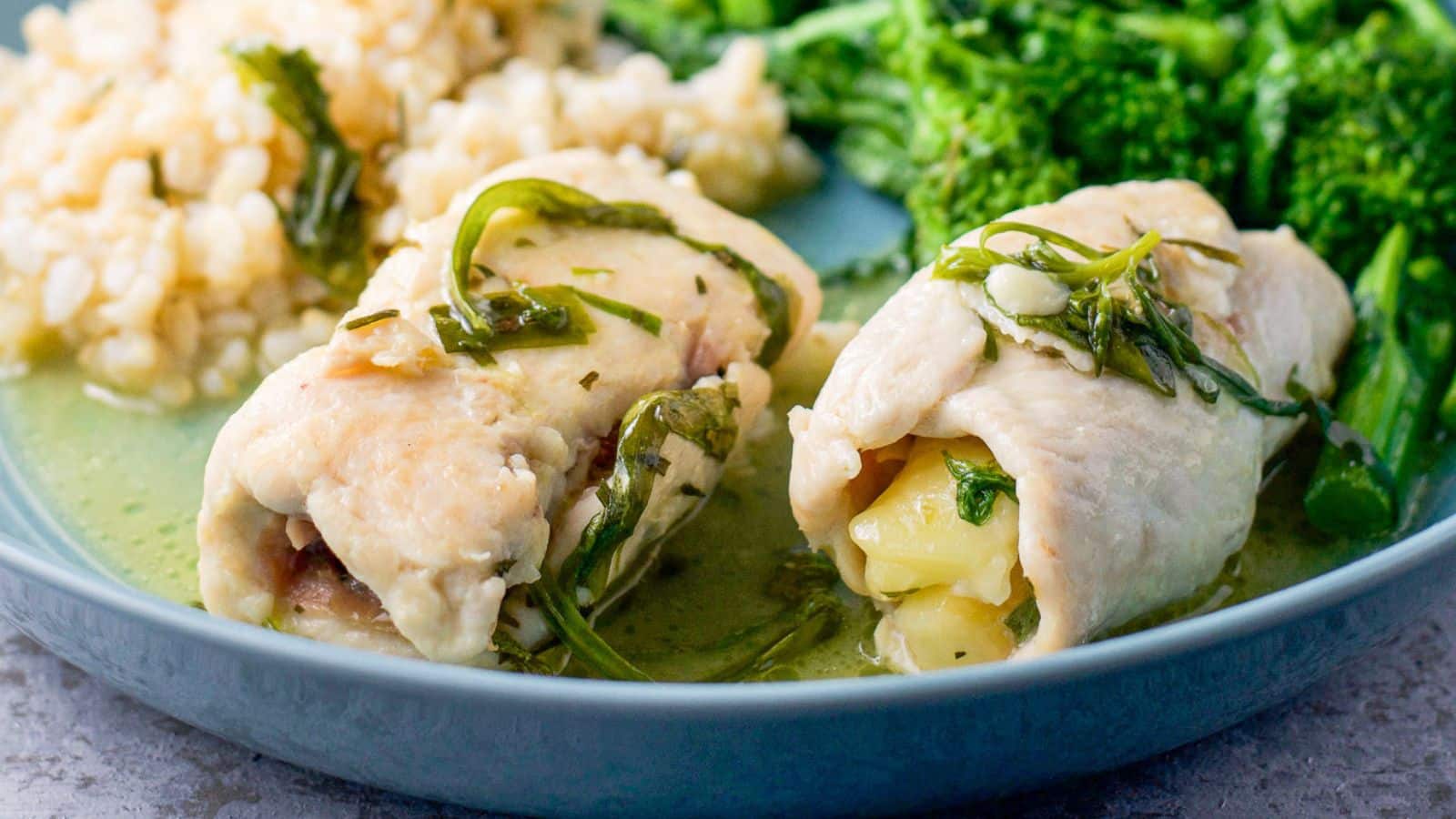 A blue plate with two chicken rolls on it along with rice and broccoli