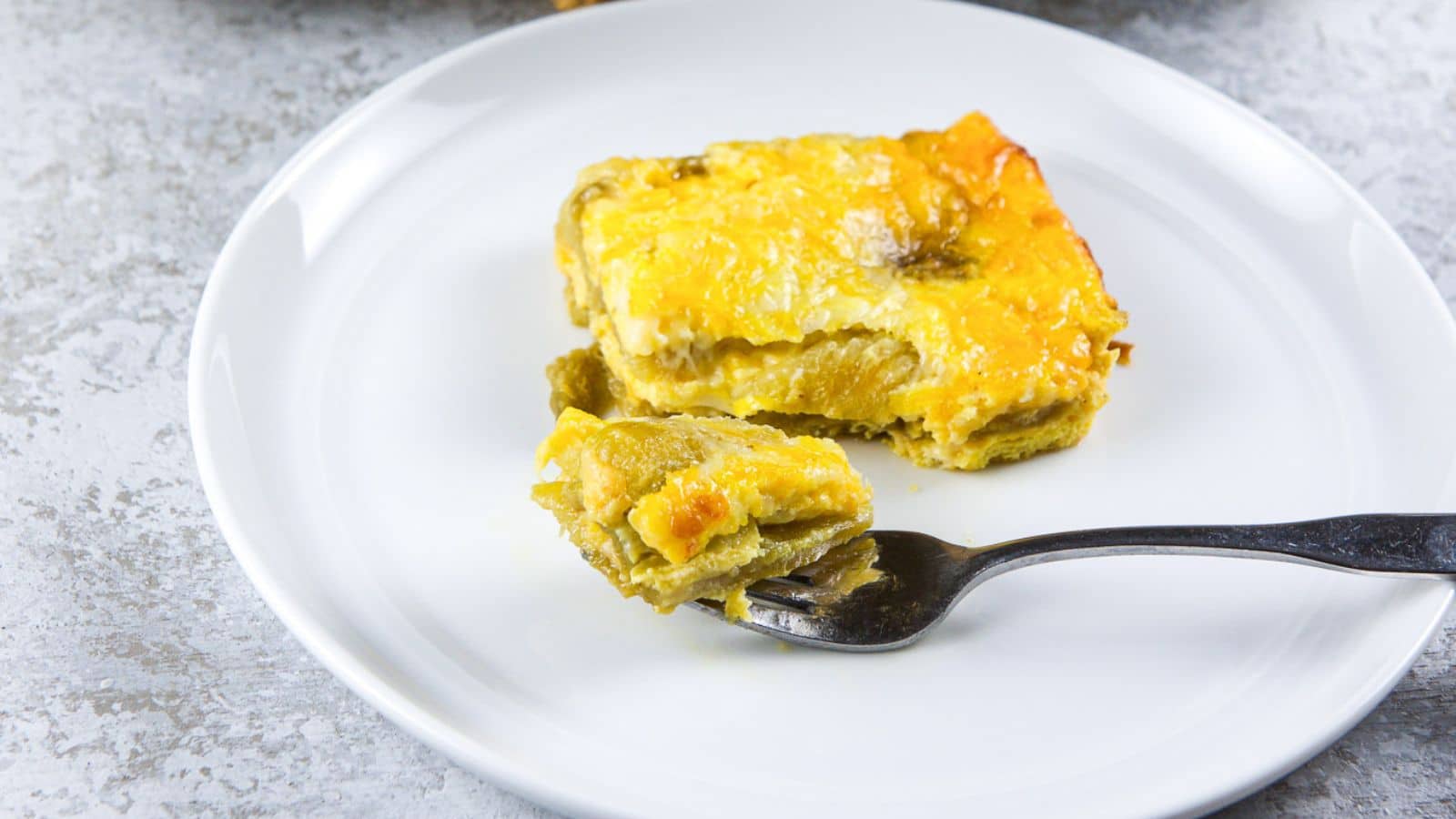 A round white plate with an egg and chile casserole with a fork with a bite on it