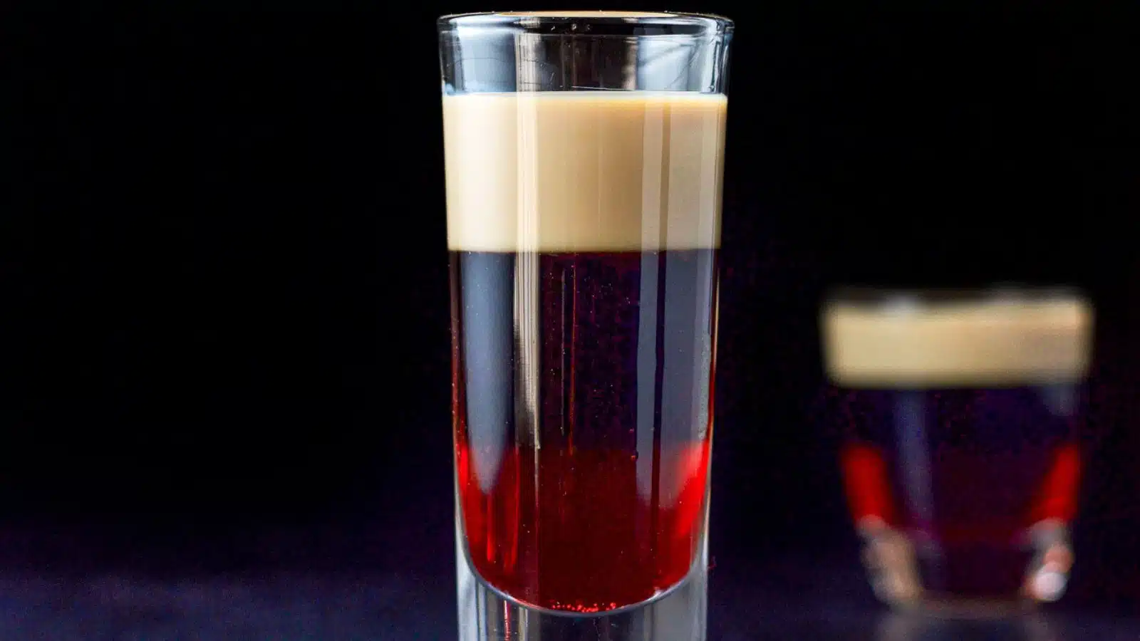a tall and short glass layered with three different colored liqueurs