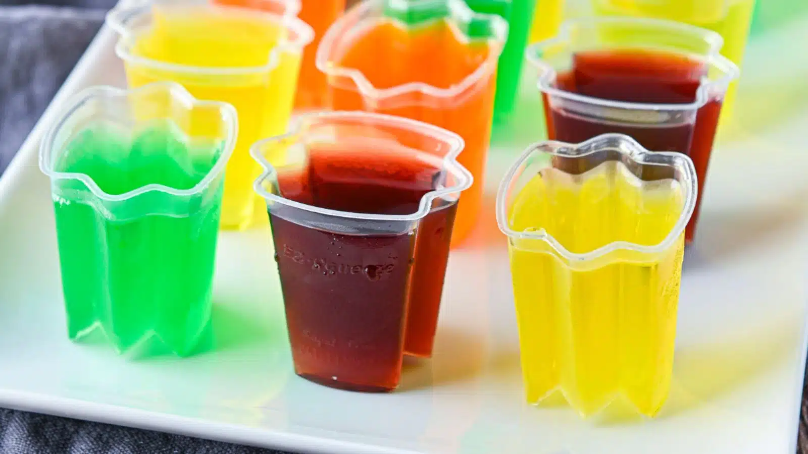 A white platter with colorful jello shots in plastic containers