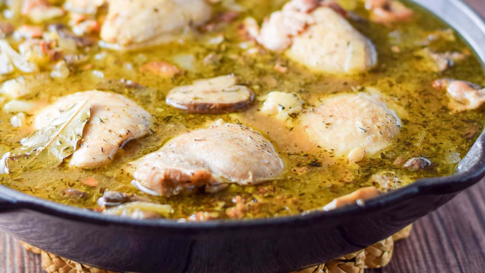 A dark pan with chicken, mushrooms, and a wine sauce in it