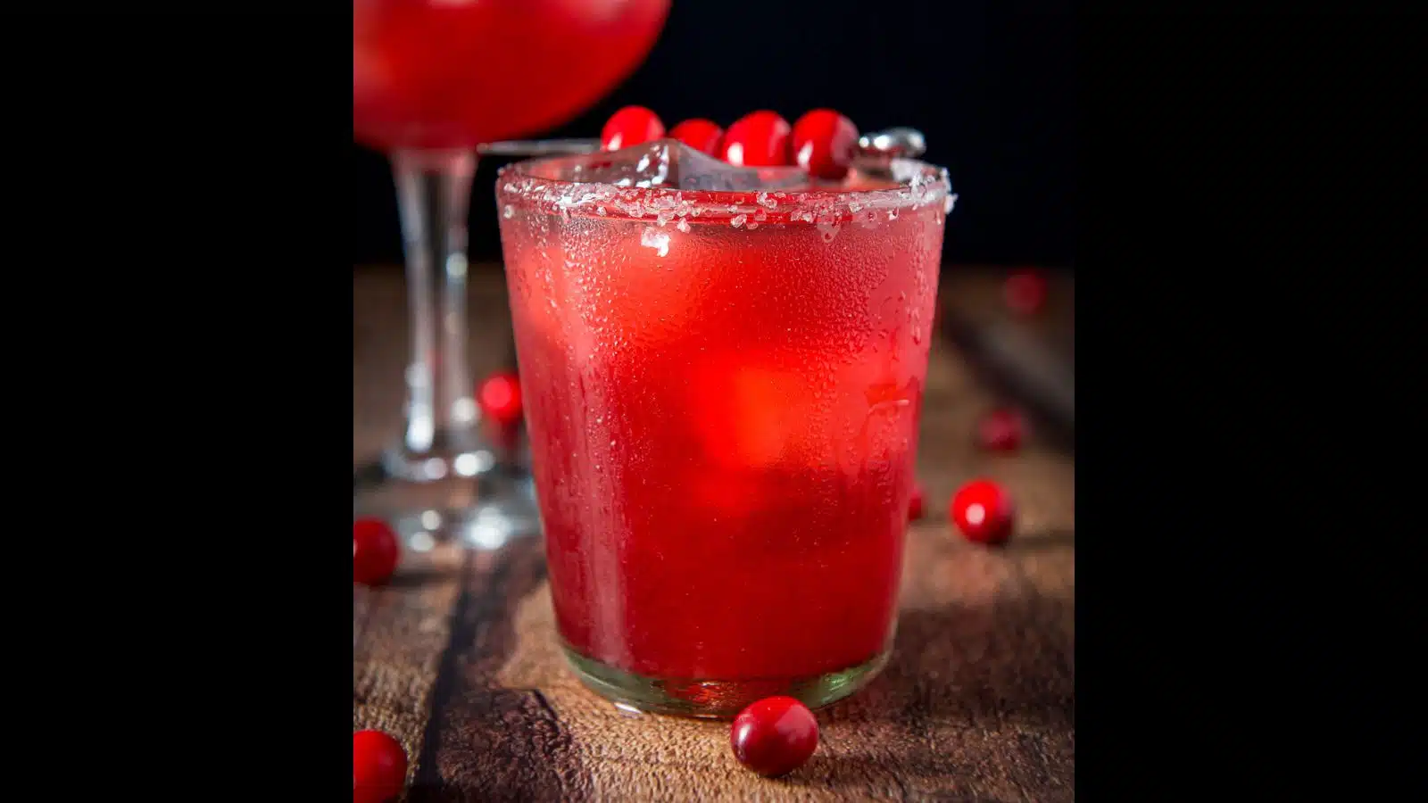 A double old fashioned glass filled with the cranberry drink with cranberries on the table and as garnish