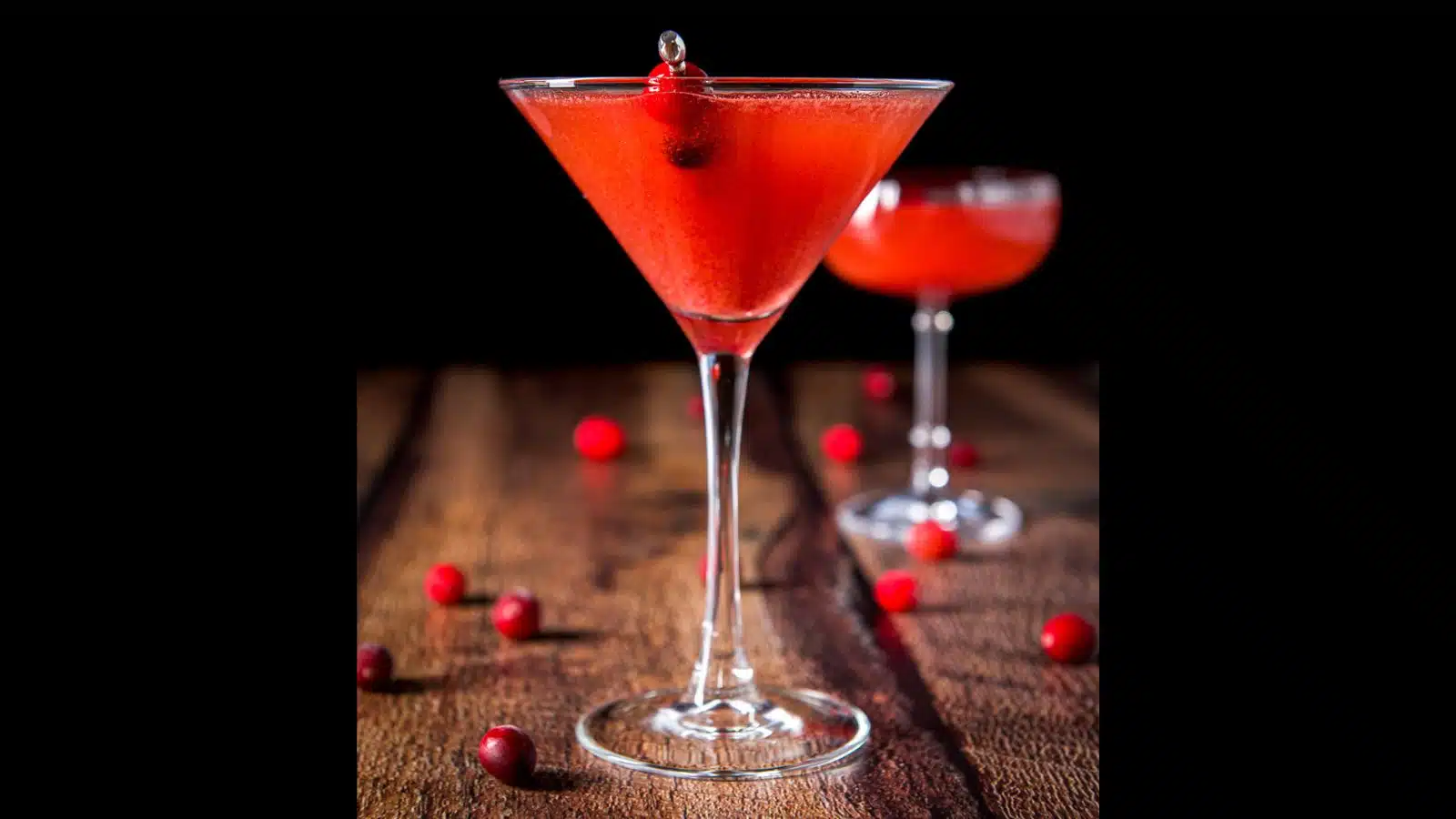 Two martini glasses filled with the cranberry martini with cranberries on a pick as garnish