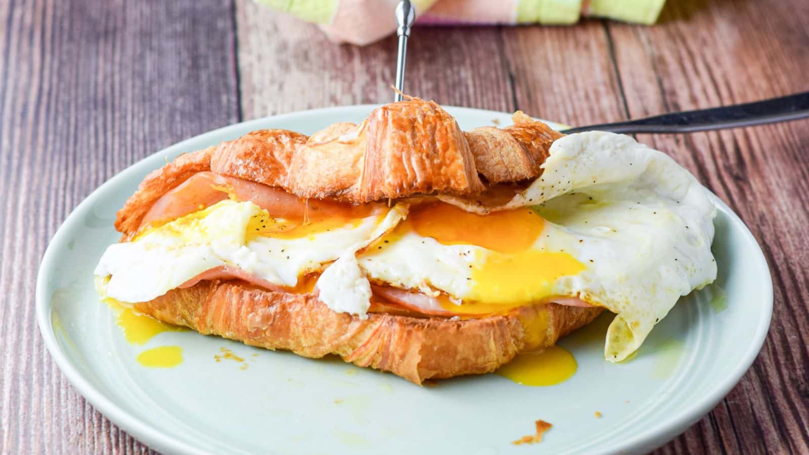 a green small plate with a croissant sandwich on it, with ham, cheese, and egg in it