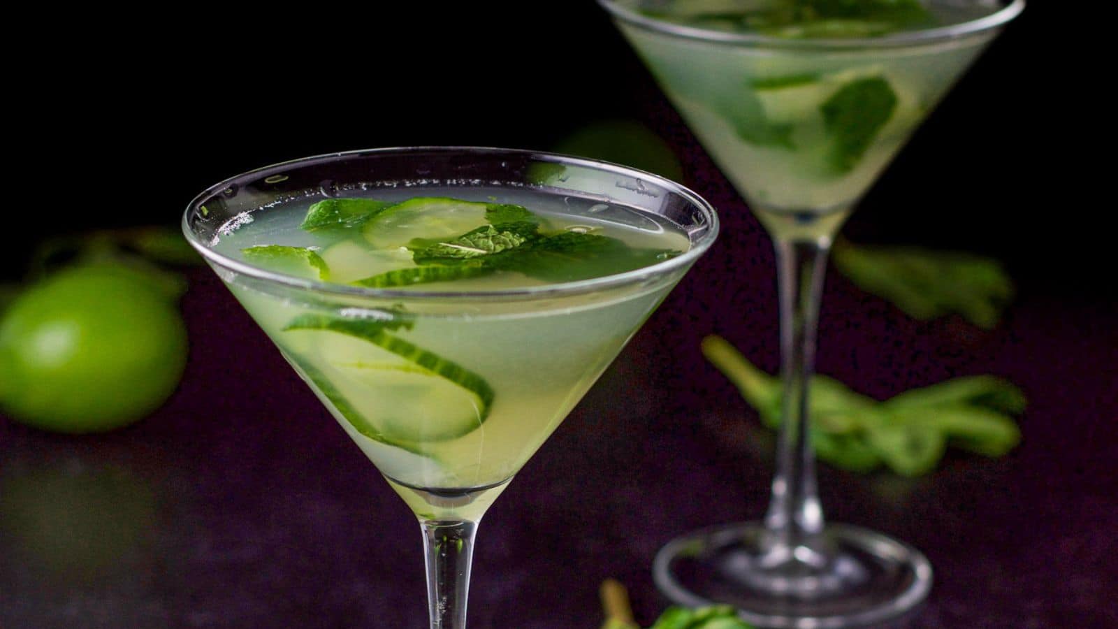 two martini glasses with the cucumber drink it it with lime, mint, and sliced cucumbers