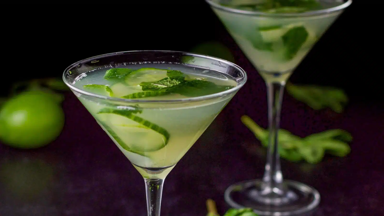 two martini glasses with the cucumber drink it it with lime, mint, and sliced cucumbers