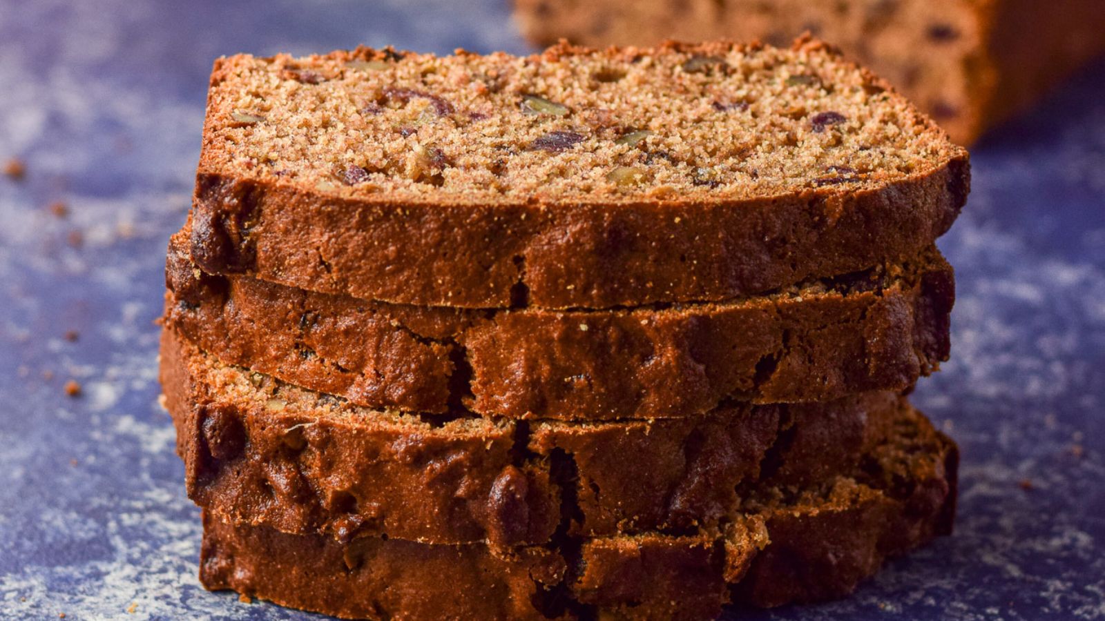 Four pieces of date nut bread piled on top of each other on a blue board