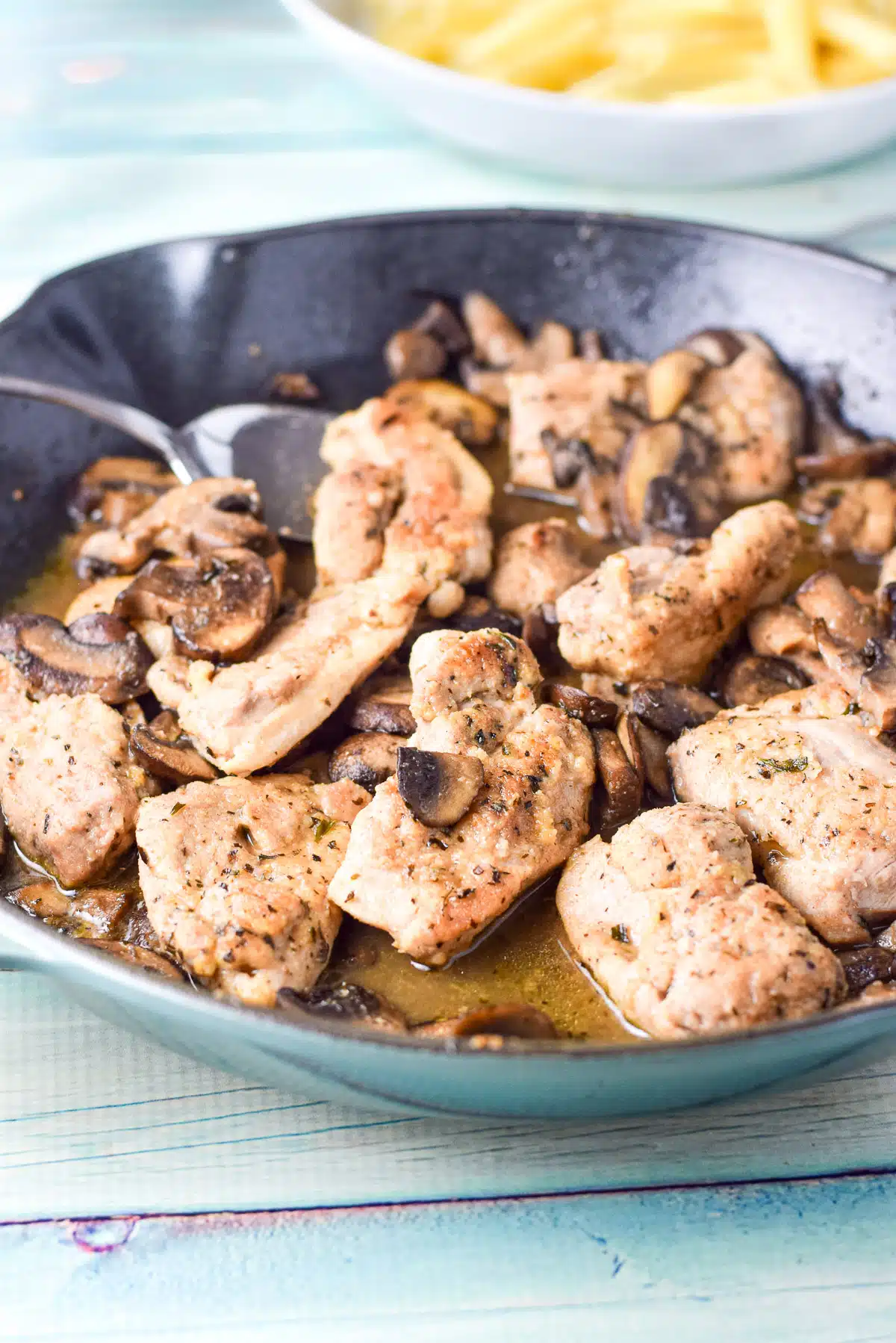 A green pan with chicken pieces, mushrooms, and a sauce