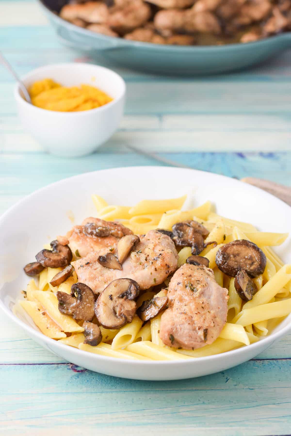 A white deep dish with pasta with chicken, sauce, and mushrooms on it