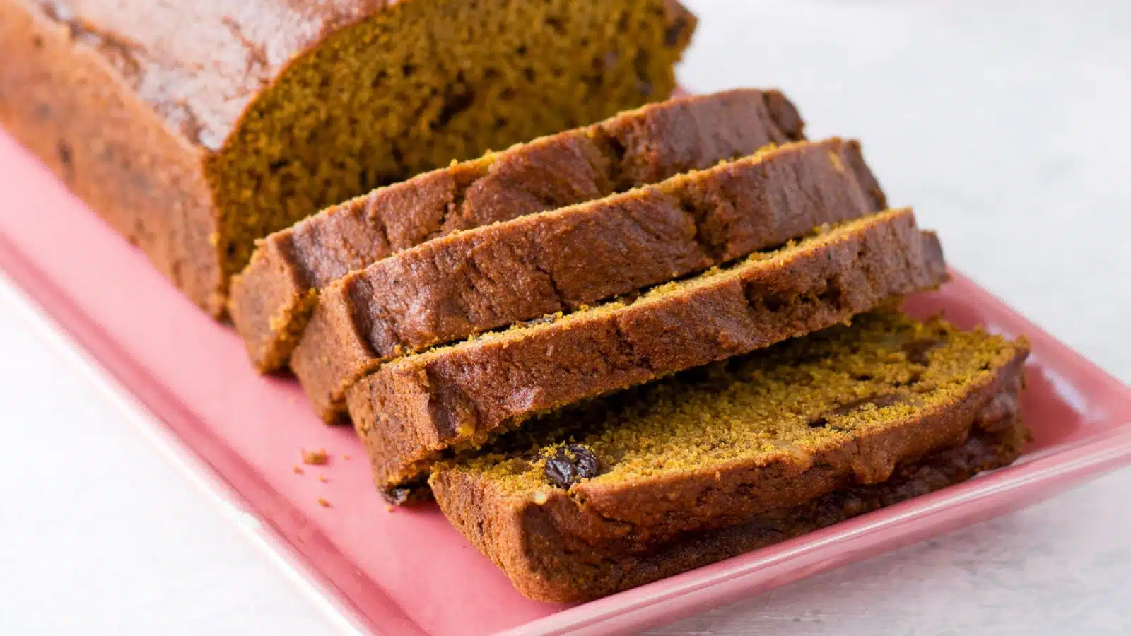 A pink platter with slices of pumpkin bread in front of the loaf