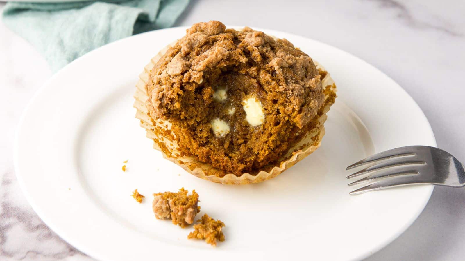A plate with a muffin with a bite taken out of it and butter melting in it