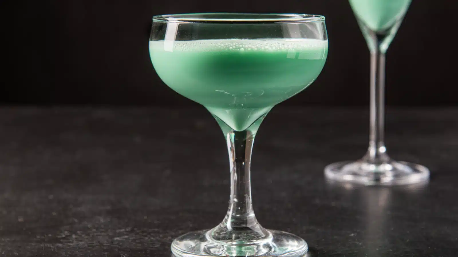 a green cocktail in a coupe glass on a dark table