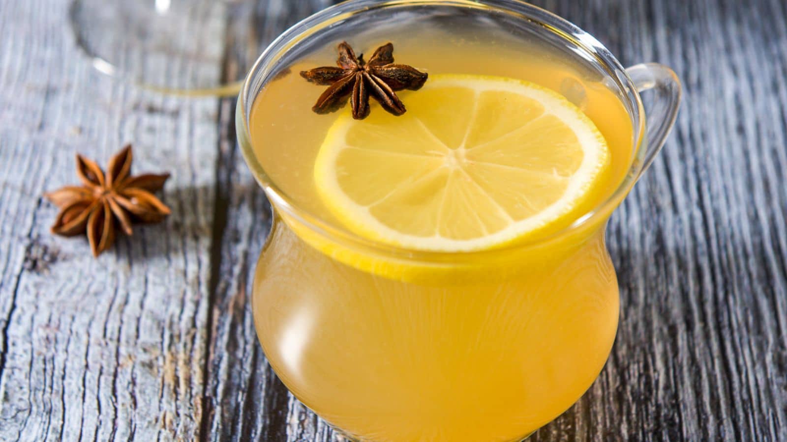 a glass tea cup with the lemon toddy in it with a lemon wheel, and star anise as garnish