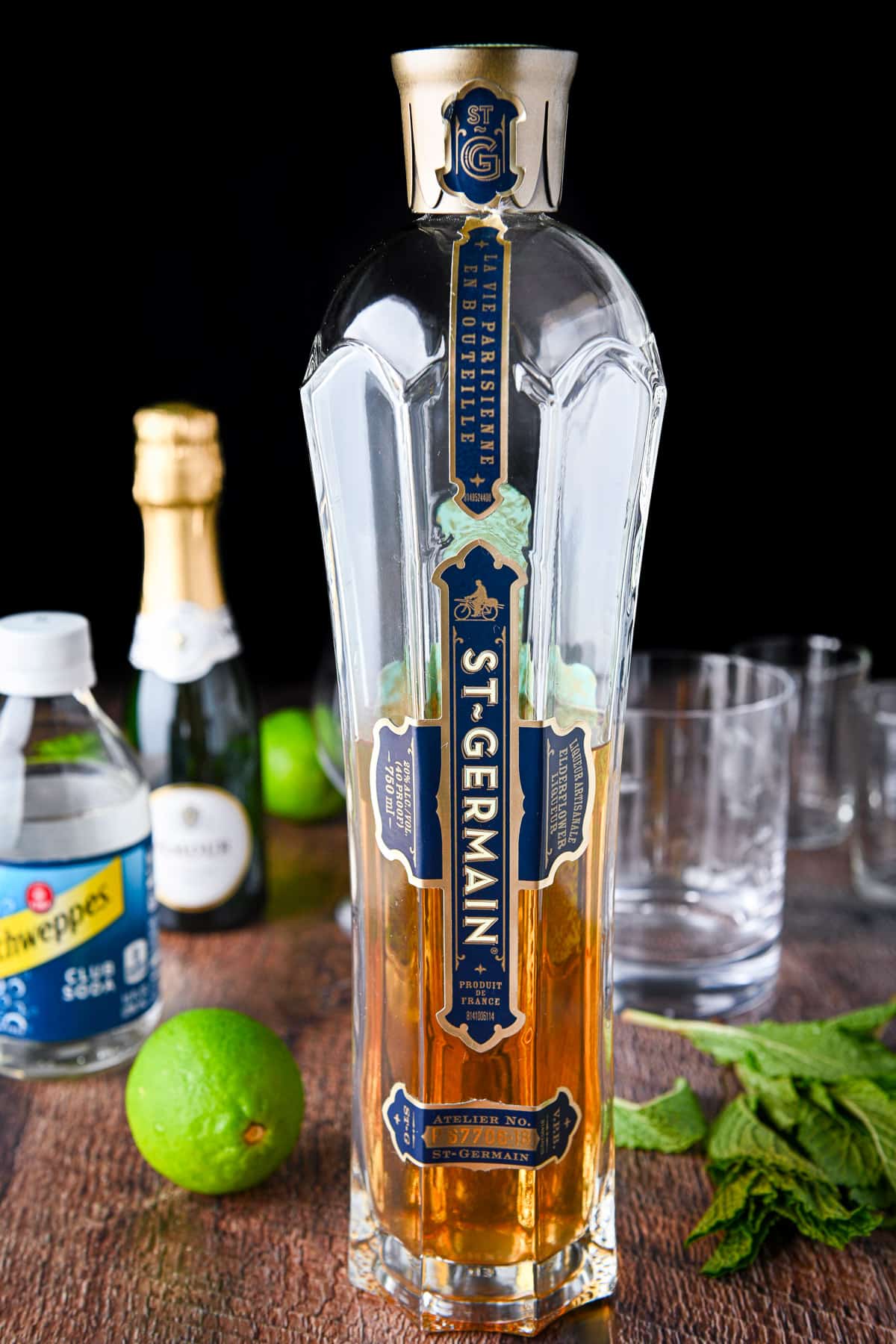 Elderberry liqueur, prosecco, lime, and club soda on the table with mint and glasses