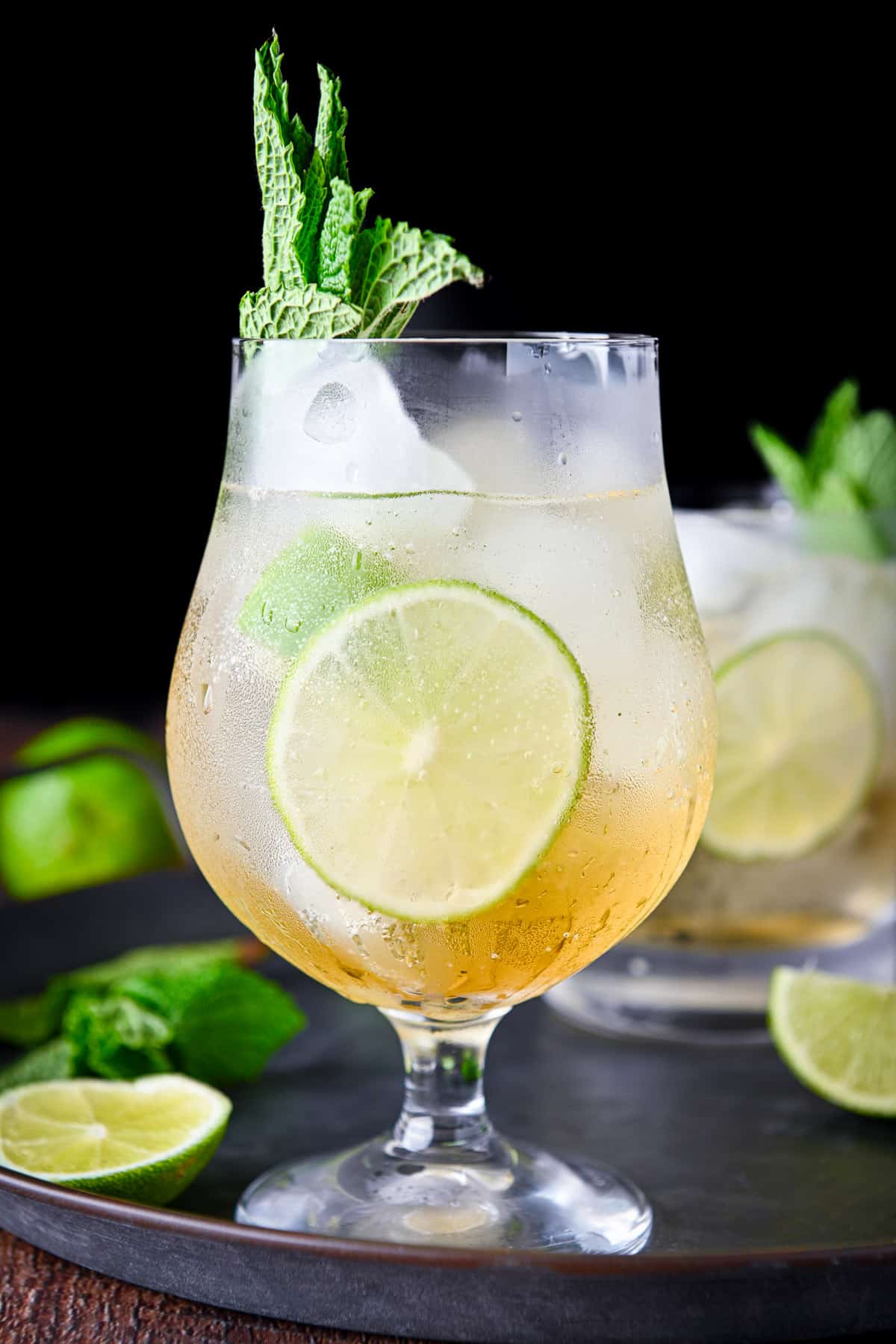 a tulip glass in front of a rocks glass filled with the cocktail with lime and mint as garnish