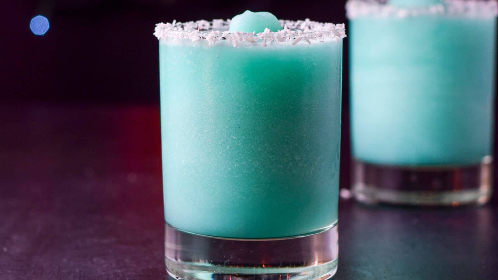 Two glasses filled with the frozen blue cocktail with coconut on the rim