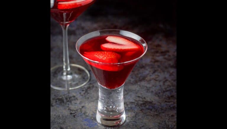 A red cocktail in martini glasses with sliced strawberries floating as garnish