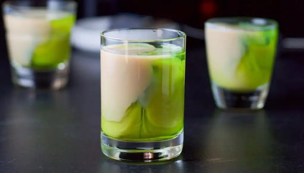 three shot glasses with a half and half - green and beige liqueur