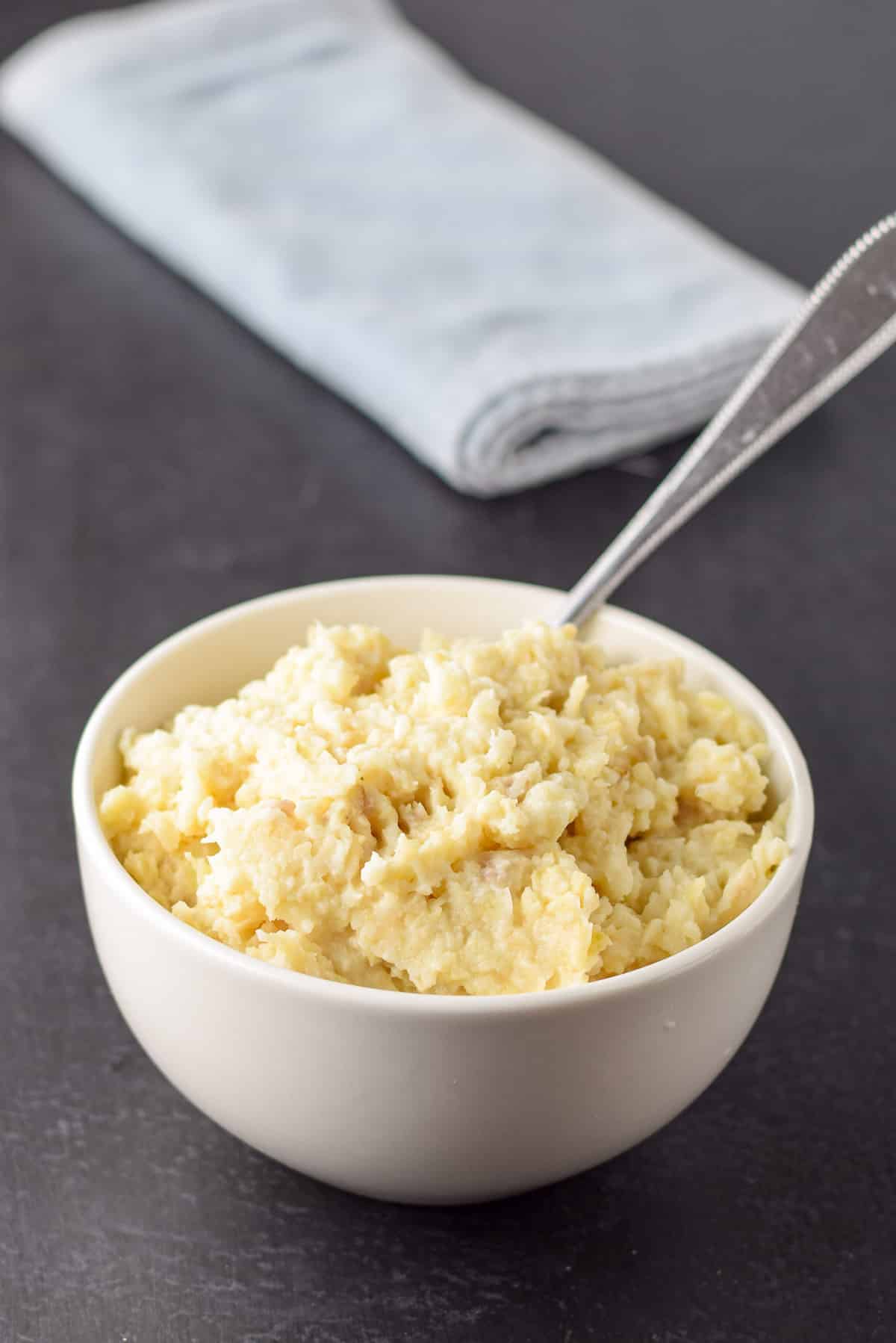 A white bowl filled with the mashed celery root and a spoon in it