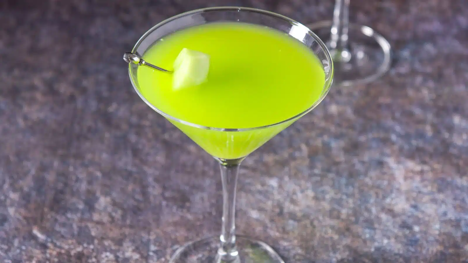 A martini glass filled with the green cocktail with some melon on a pick