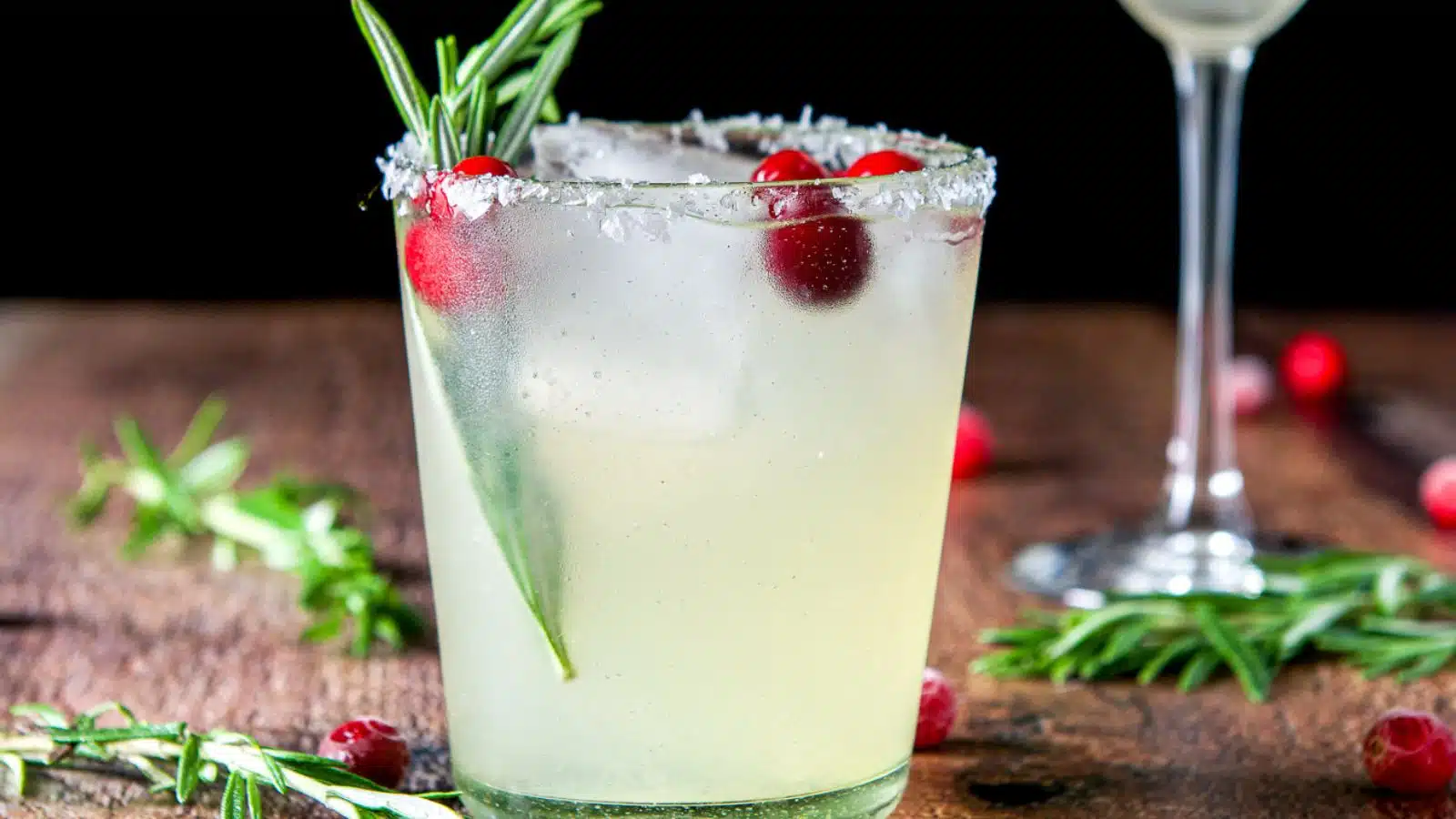 A salt rimmed glass filled with the margarita with rosemary and cranberries in it