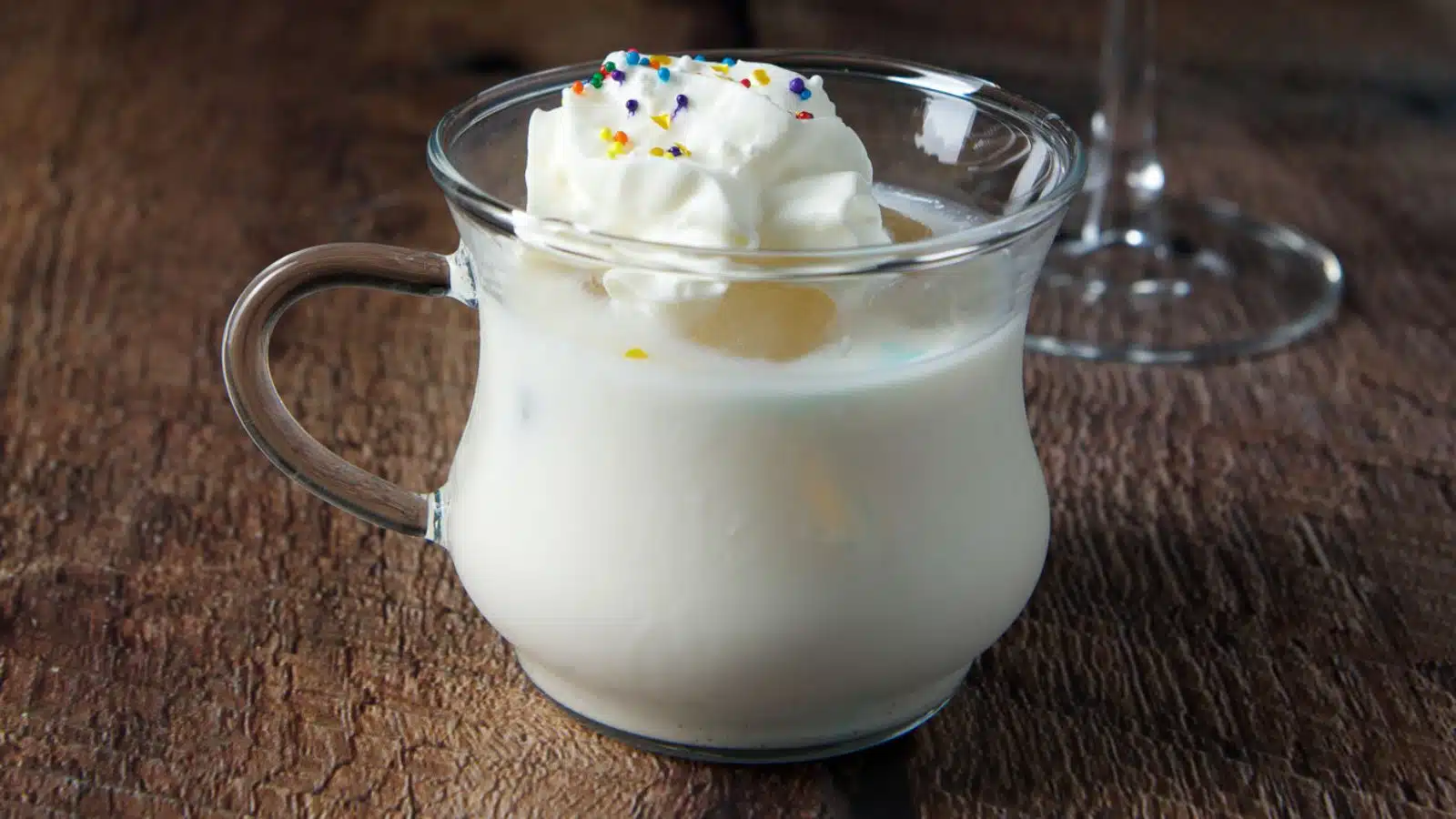 A glass with a handle with a cream cocktail in it with whipped cream and sprinkles