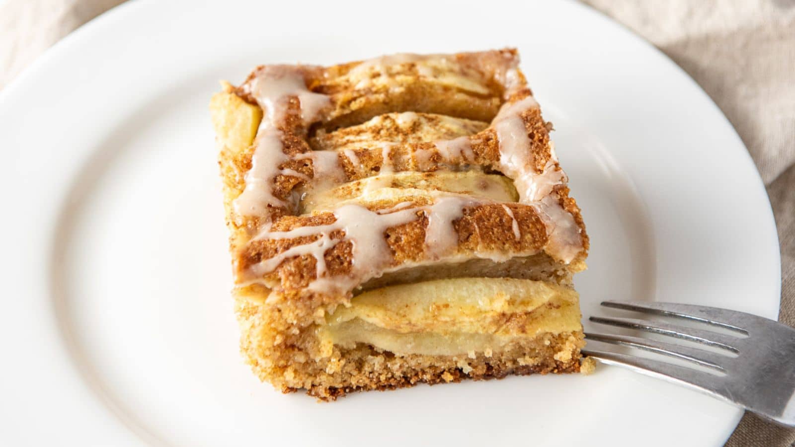 A white plate with a fork on it along with a piece of apple cake