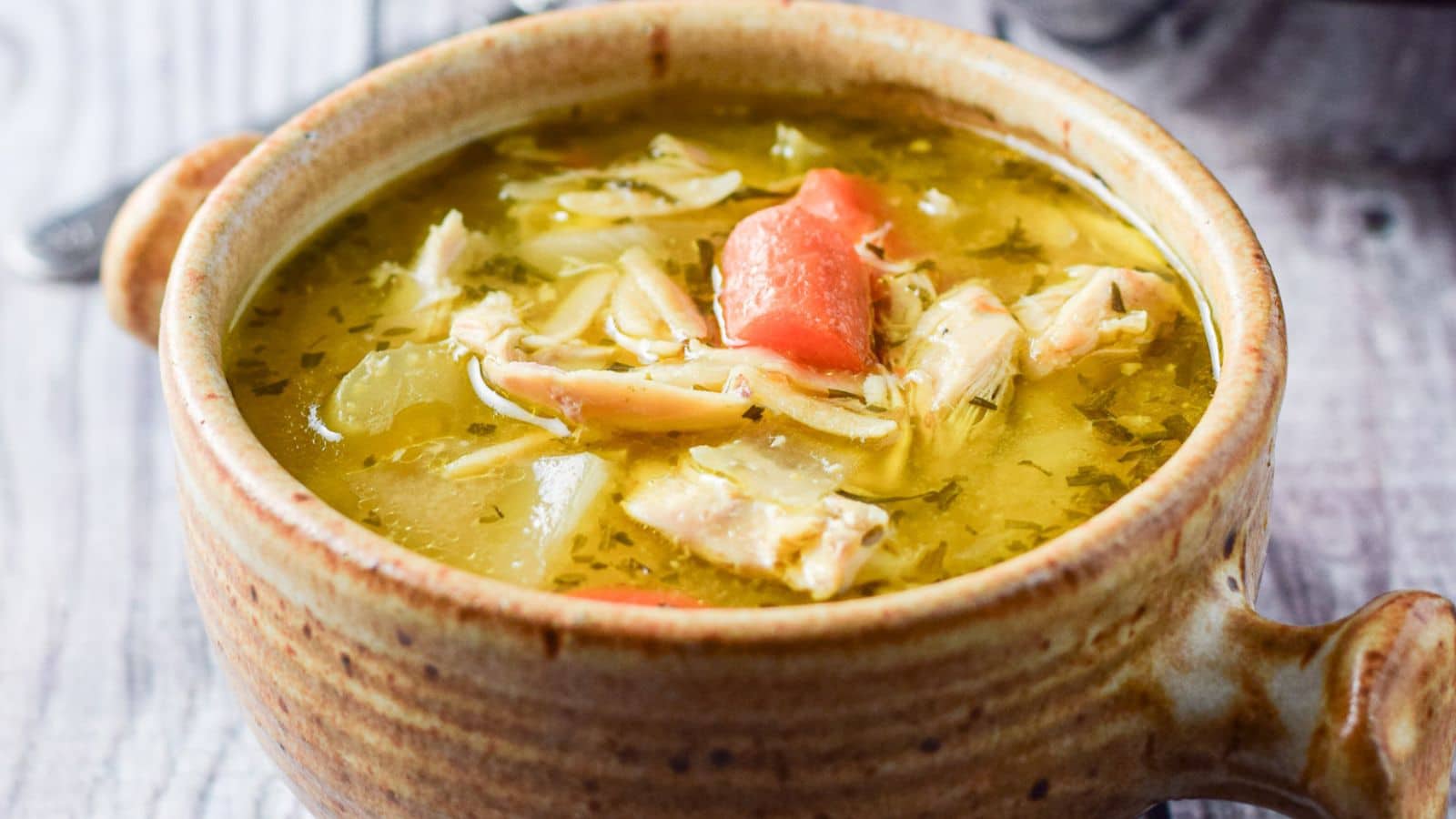 a crock filled with chicken soup with carrots floating in it