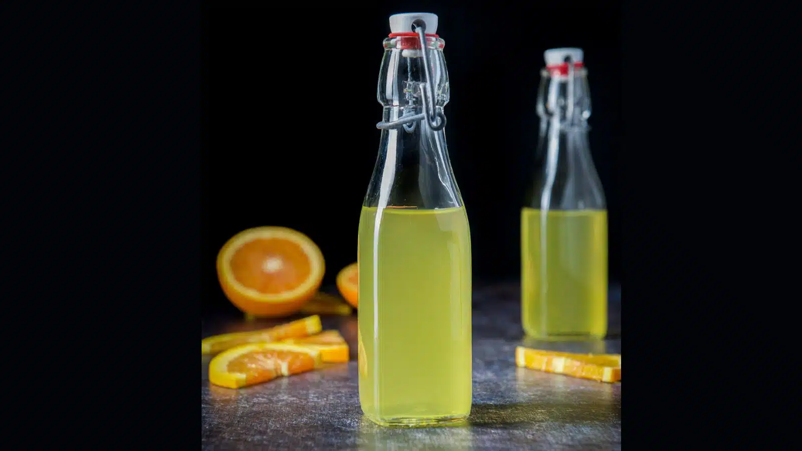 two glass bottles with stoppers filled with orange vodka with orange slices in the background