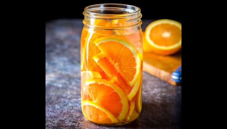 A jar filled with orange slices and vodka with a board with an orange in the back