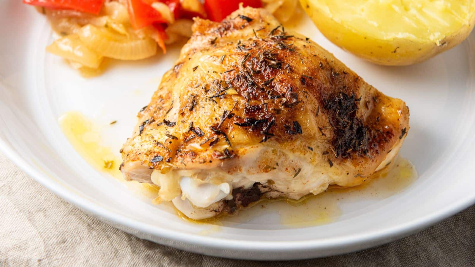 A white plate with a chicken thigh on it with vegetables and potato