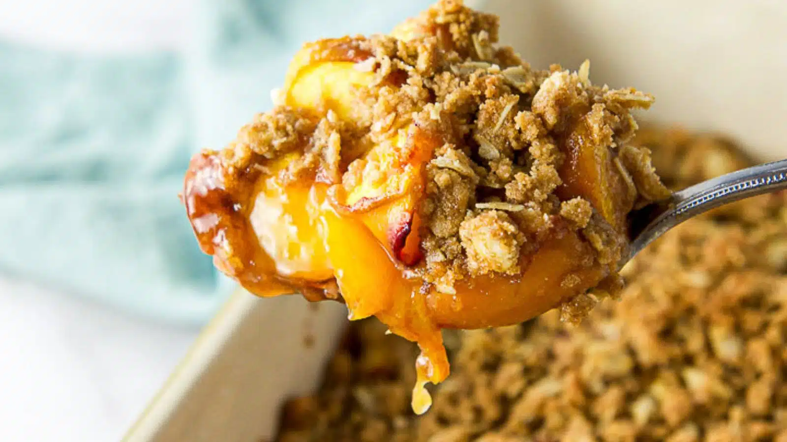 A spoon with peach crisp on it over the pan of crisp