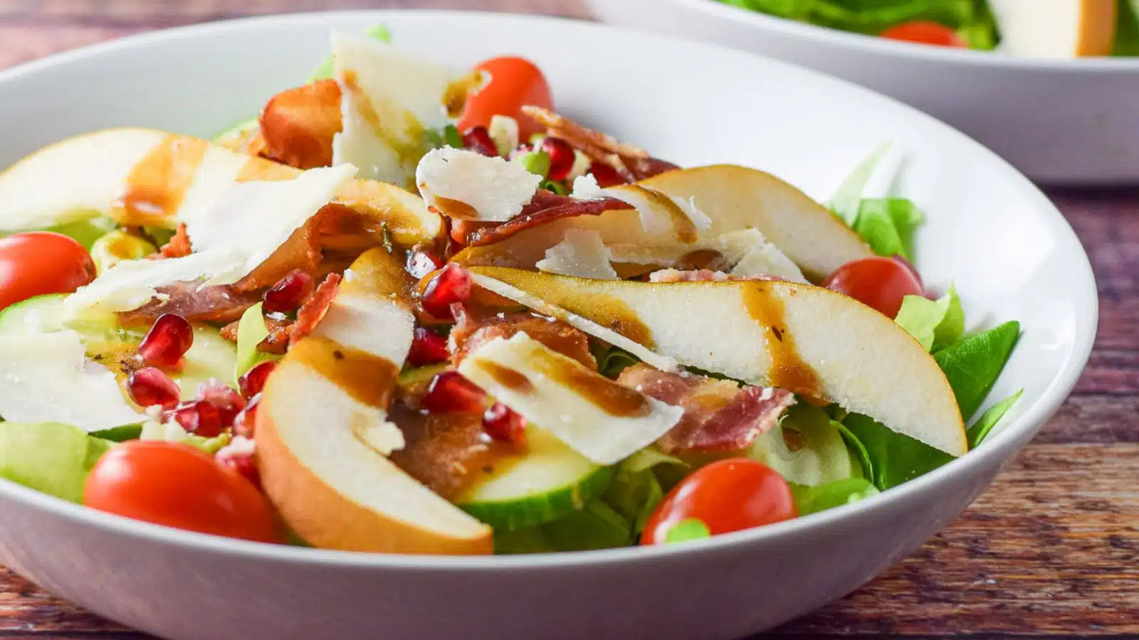 a white deep plate with pears on a salad with pomegranates, bacon, and dressing