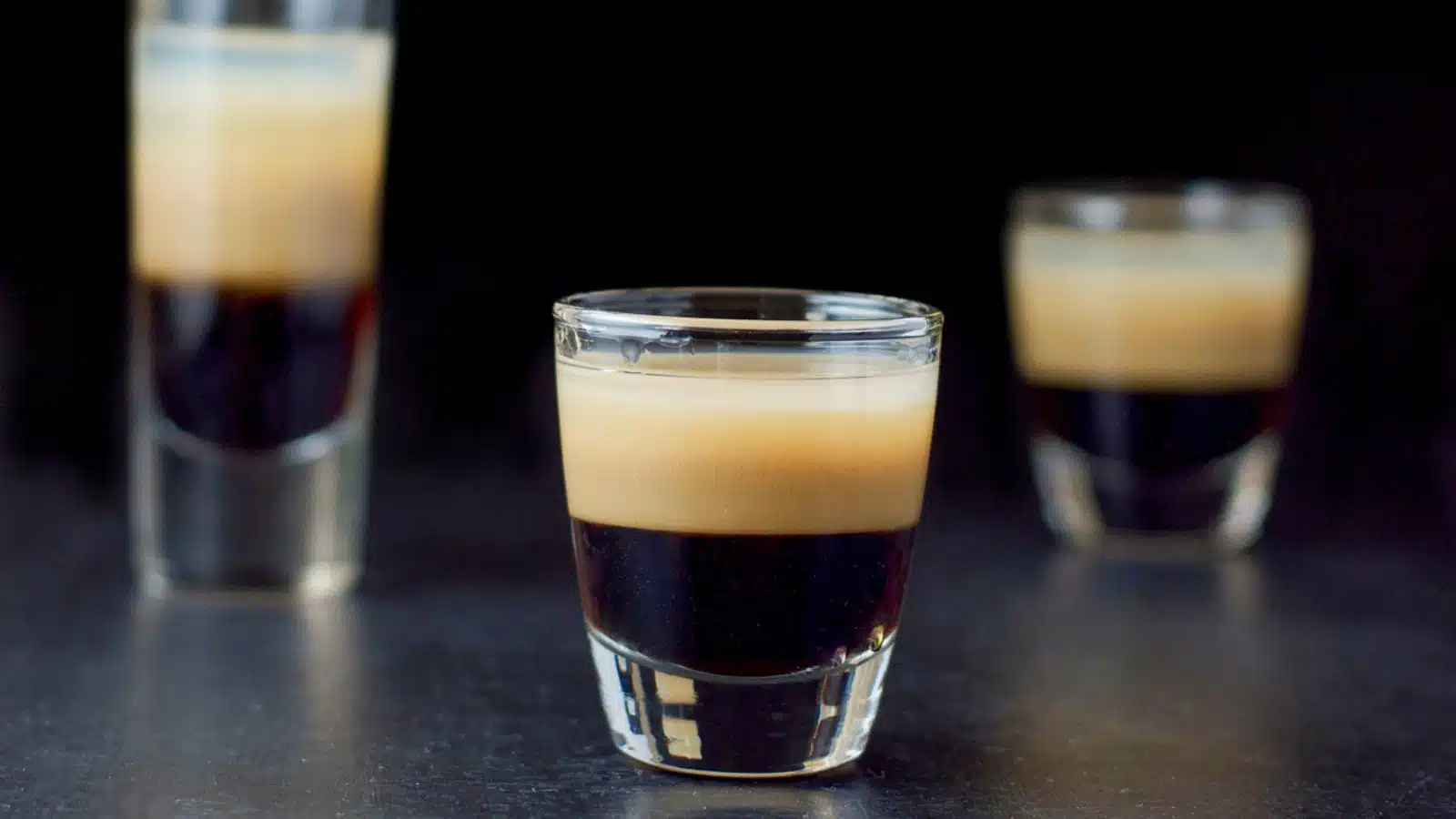 Three glasses layered with a dark, beige and clear liqueur