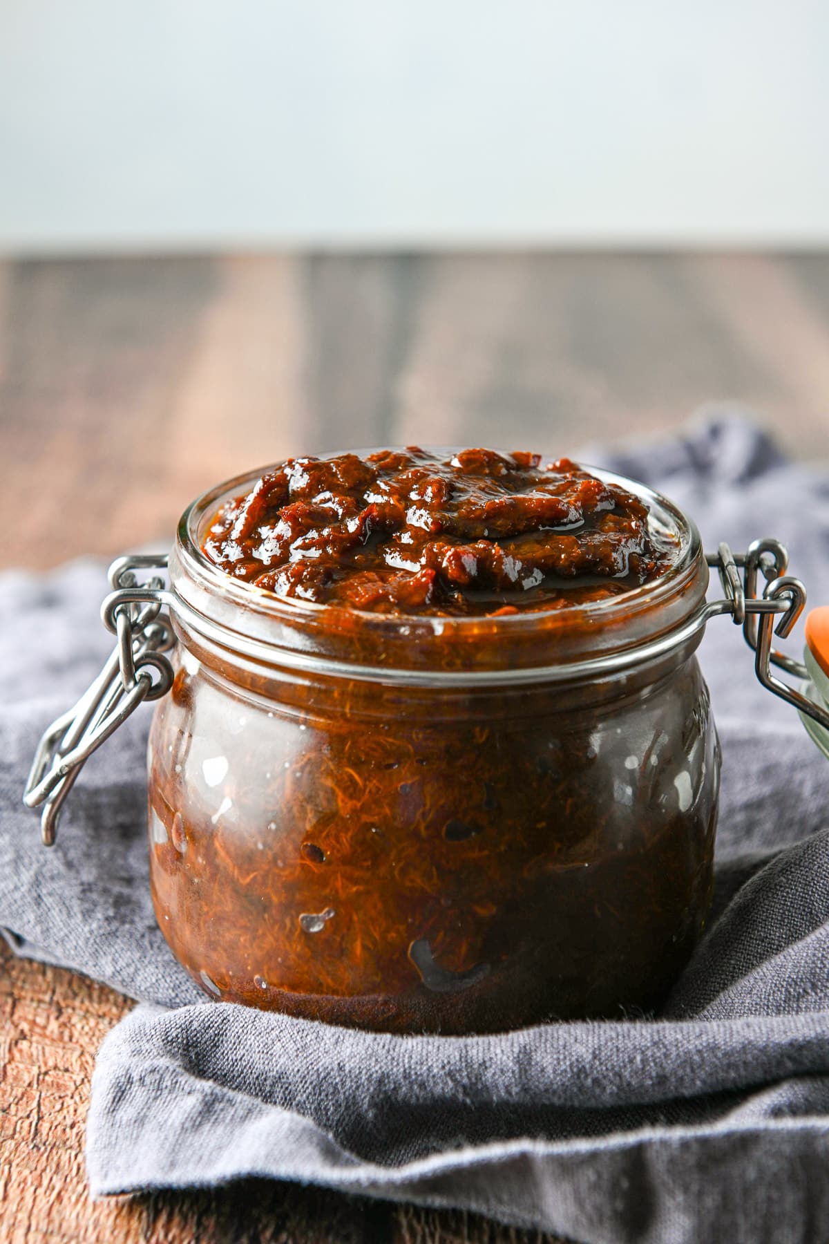 A wooden table with a grey napkin on it with a jar filled with the prune spread