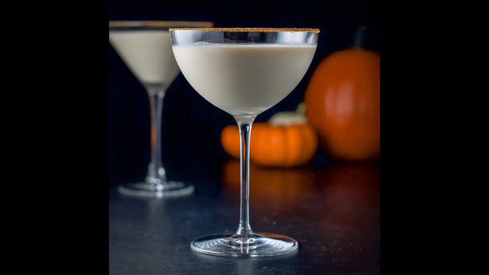 Two martini glasses filled with the cream cocktail with pumpkin spice on the rims and pumpkins in the background