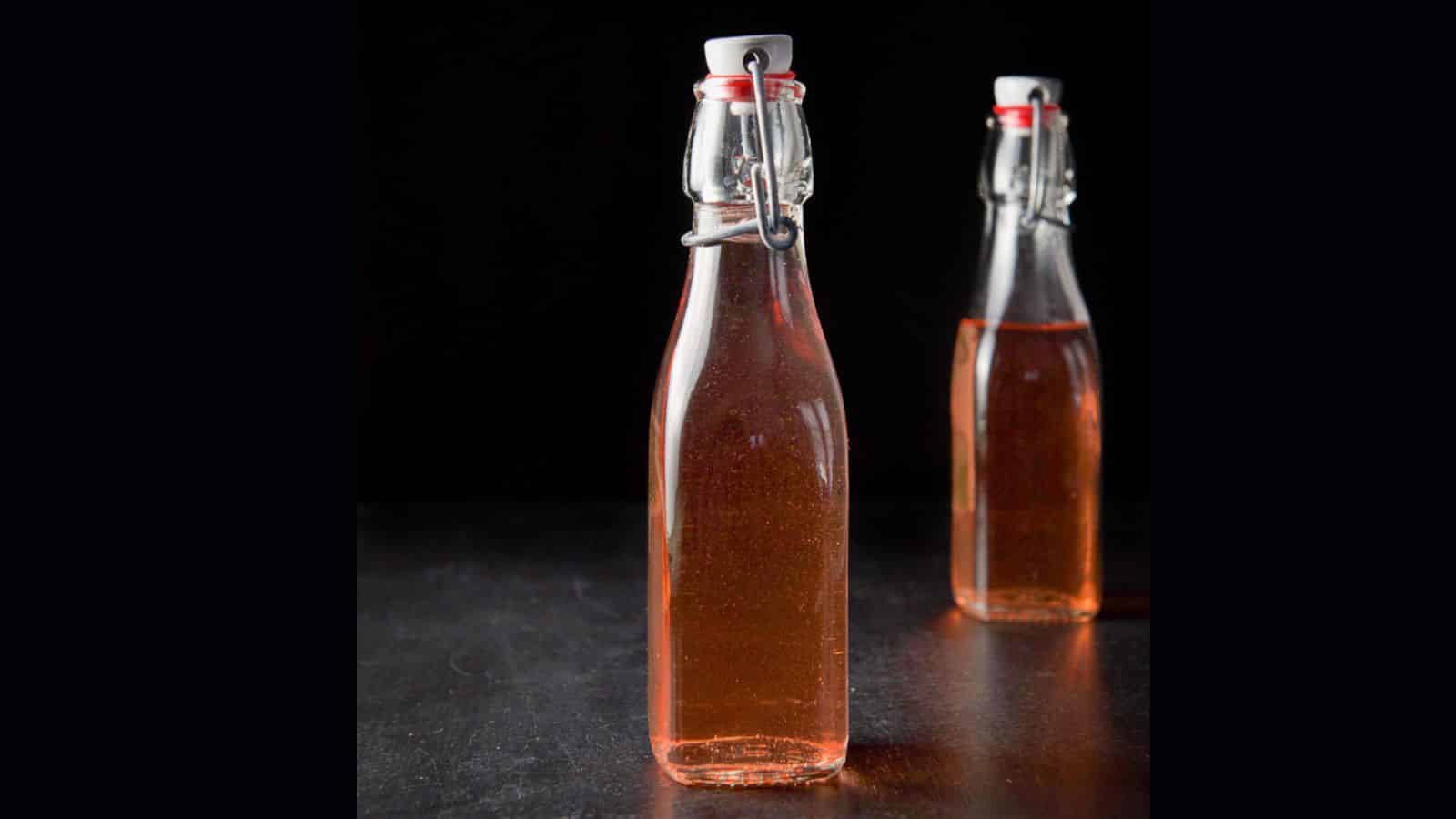 Two small glass bottles with white tops filled with homemade rhubarb vodka