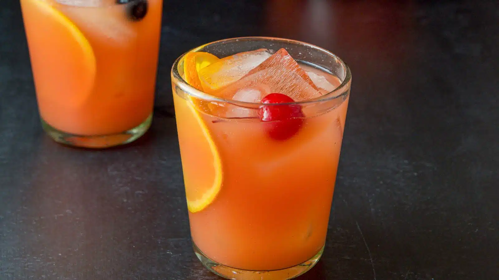 Two glasses with the orange-red cocktail with cherries and orange wheels as garnish