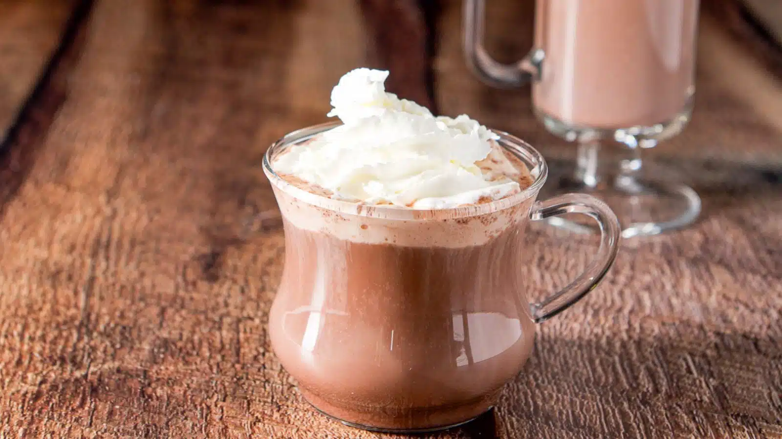A glass tea cup with a hot chocolate drink and whipped cream on top