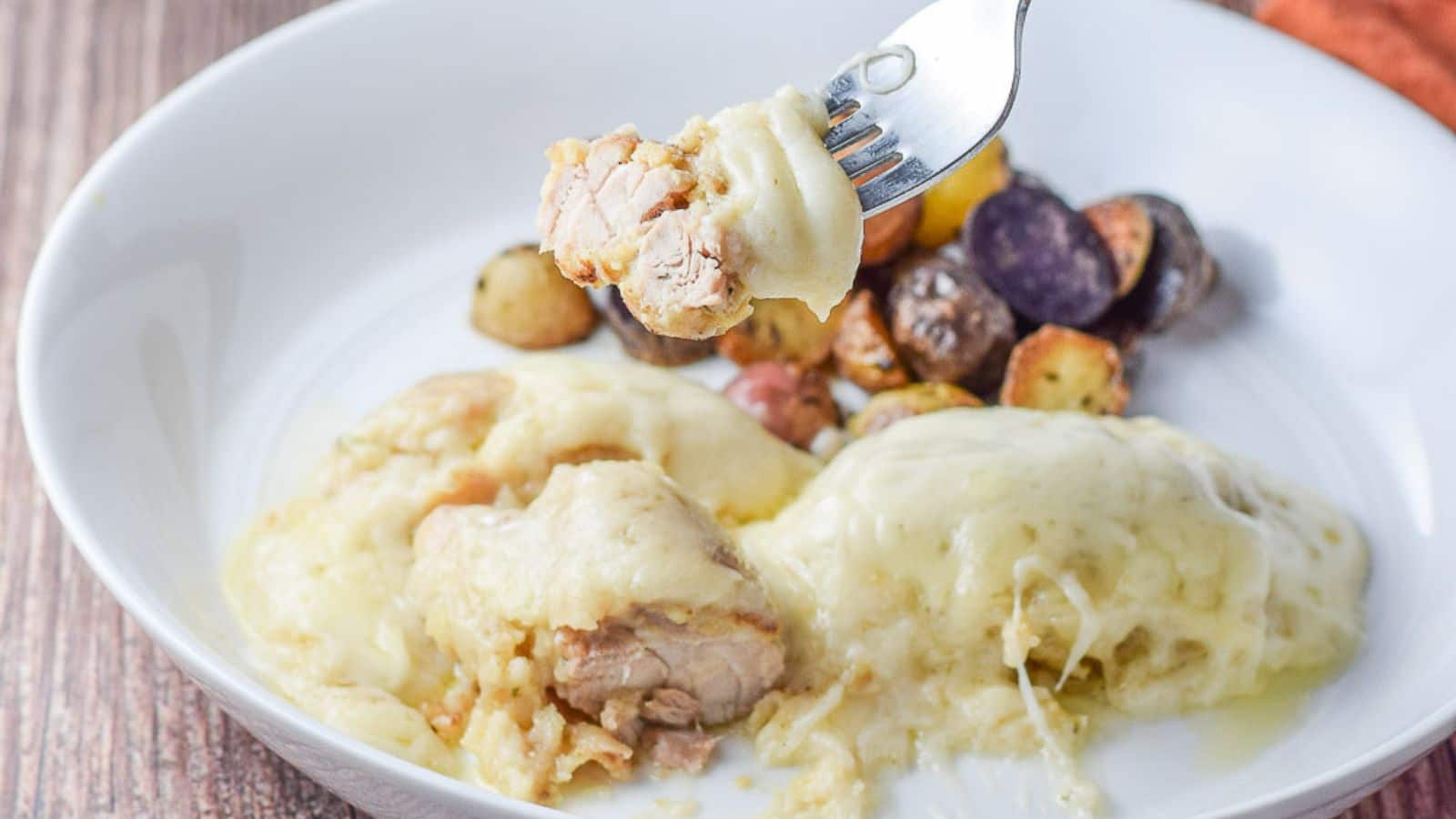 a fork with some chicken and swiss cheese on it over the plate with the chicken and potatoes