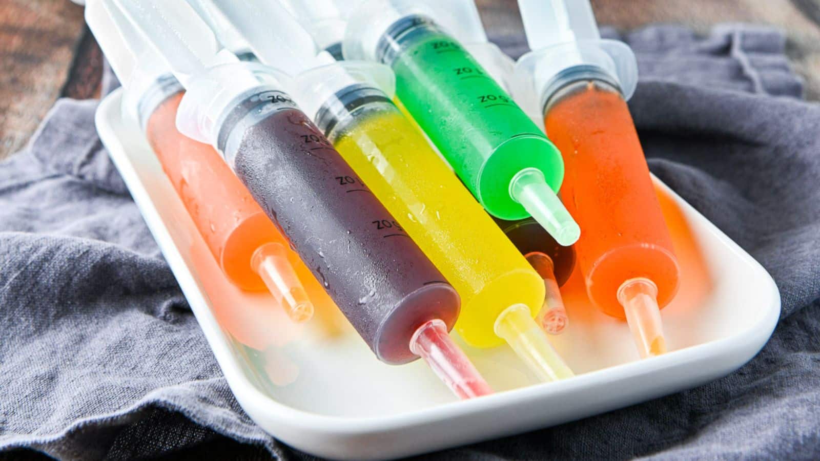 A white platter with large syringes filled with colorful jello