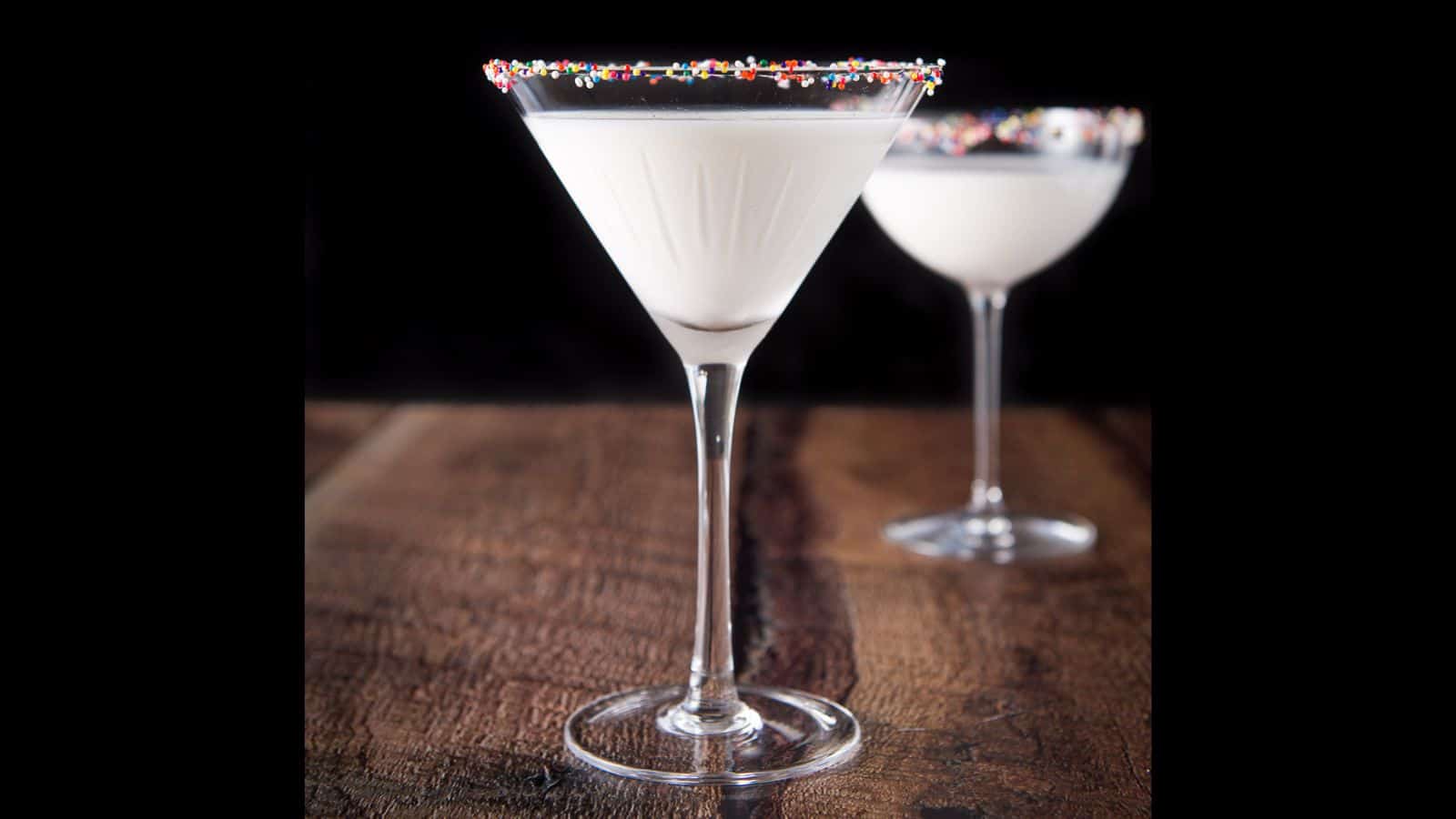 Two martini glasses with color balls on the rim filled with a white cocktail