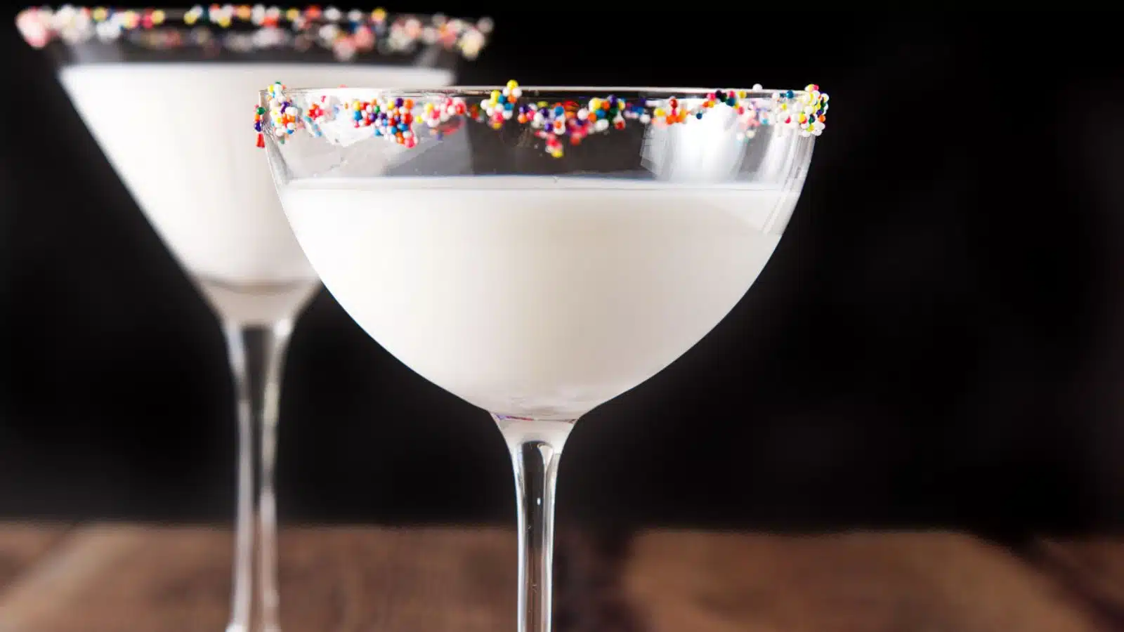 two martini glasses, one classic and one bowl filled with the white cocktail with colorful balls as garnish on the rim