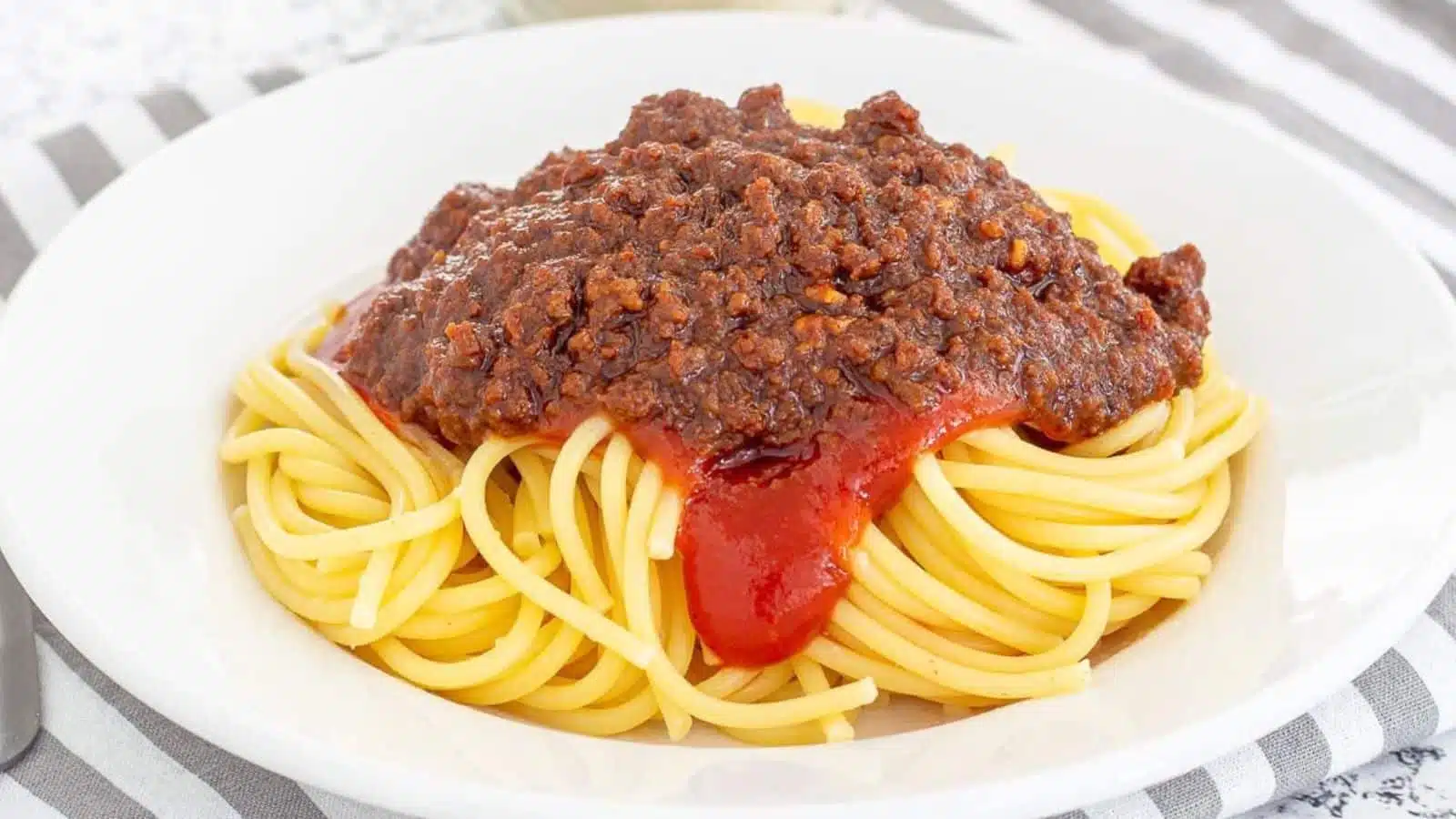 Spaghetti with tomato sauce and ground beef on it - all in a white bowl